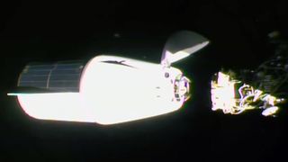 a white spacecraft with a solar array panel covering one half of its trunk approaches docking with a space station