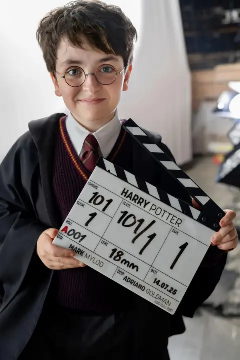 Aidan Monaghan/HBO A young boy, Dominic McLaughlin, dressed as Harry Potter holding a clipboard which says "Harry Potter" on it.