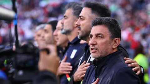 Amir Ghalenoei coach of Iran sings the national anthem
