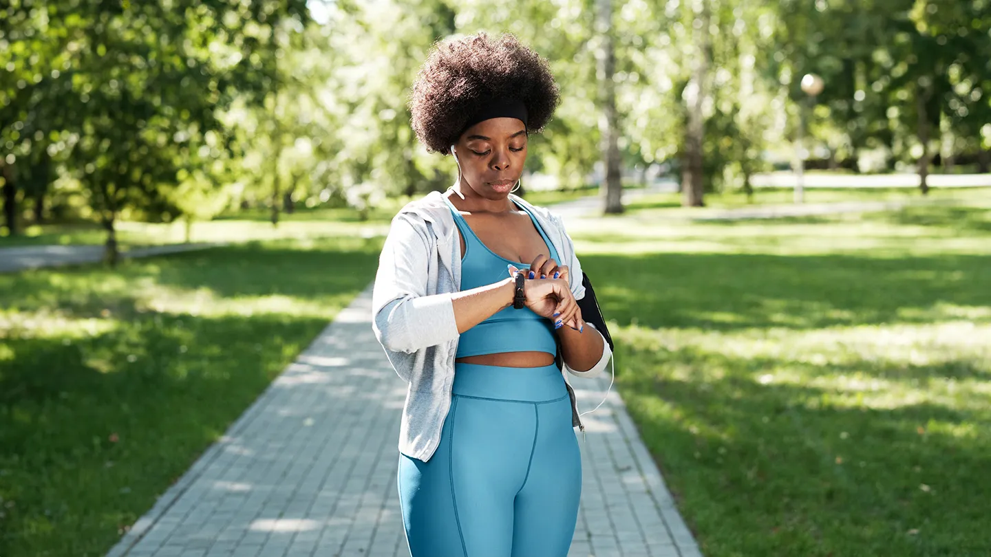 woman in park in exercise outfit looking at speedometer watch after increase in cardio exercise walking jogging running