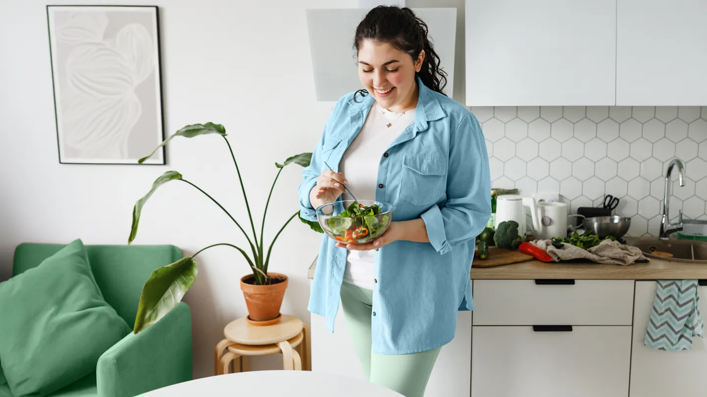 woman eating a salad standing in her kitchen