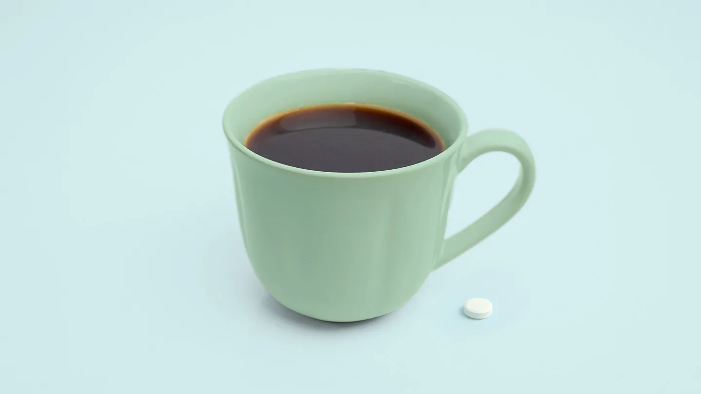 Cup of black coffee with pill next to it