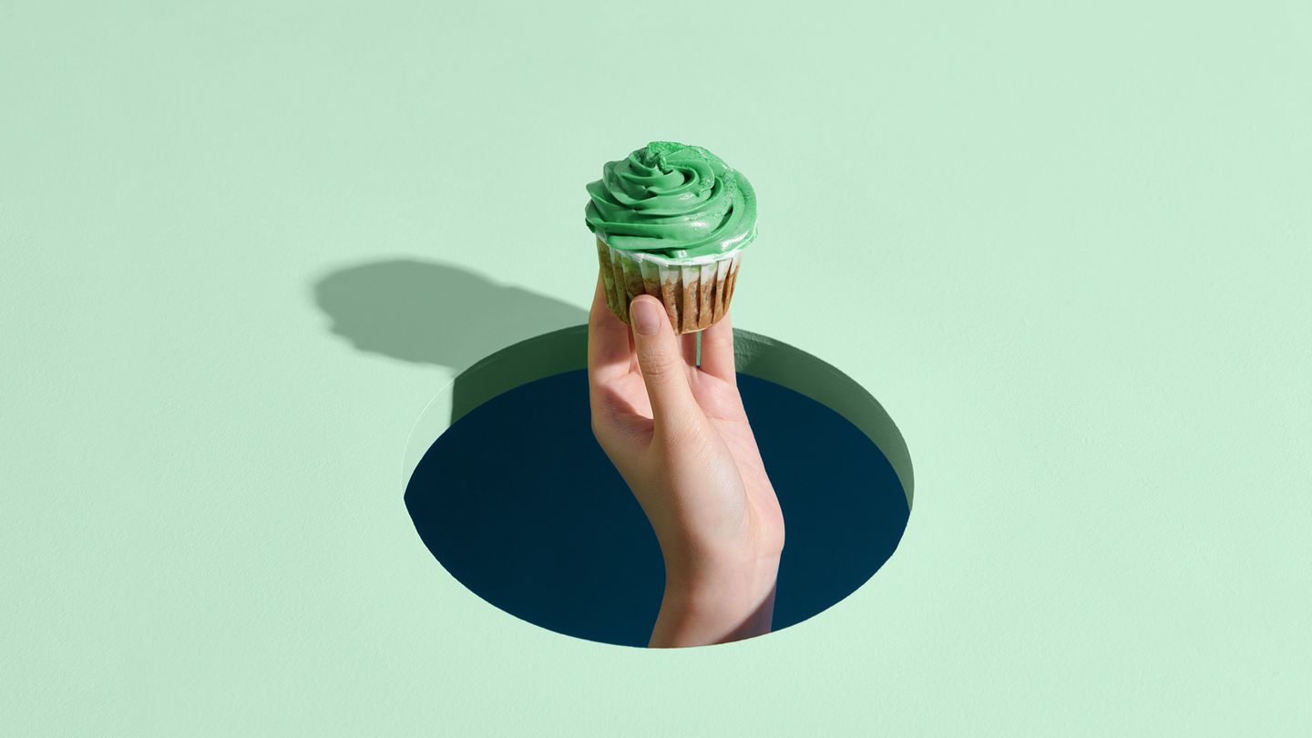 hand holding tasty cupcake through a hole in the floor